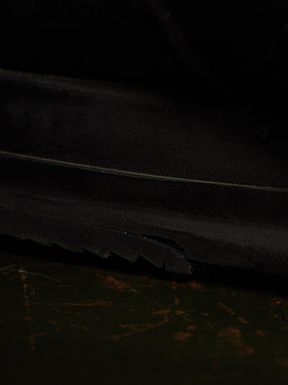 Close-up of a black rubber sole with a visible crack along the edge, resting on a dark, worn surface.