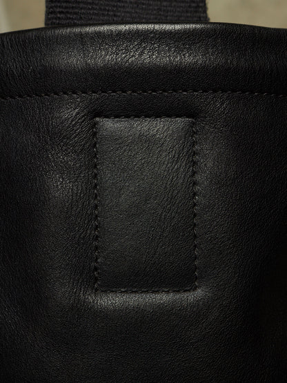 Close-up detail of a black leather bag showing a stitched rectangular patch and part of a dark strap.