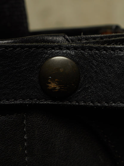 Close-up of a black leather strap with a round dark metal snap button, showing the textured leather surface and stitching.