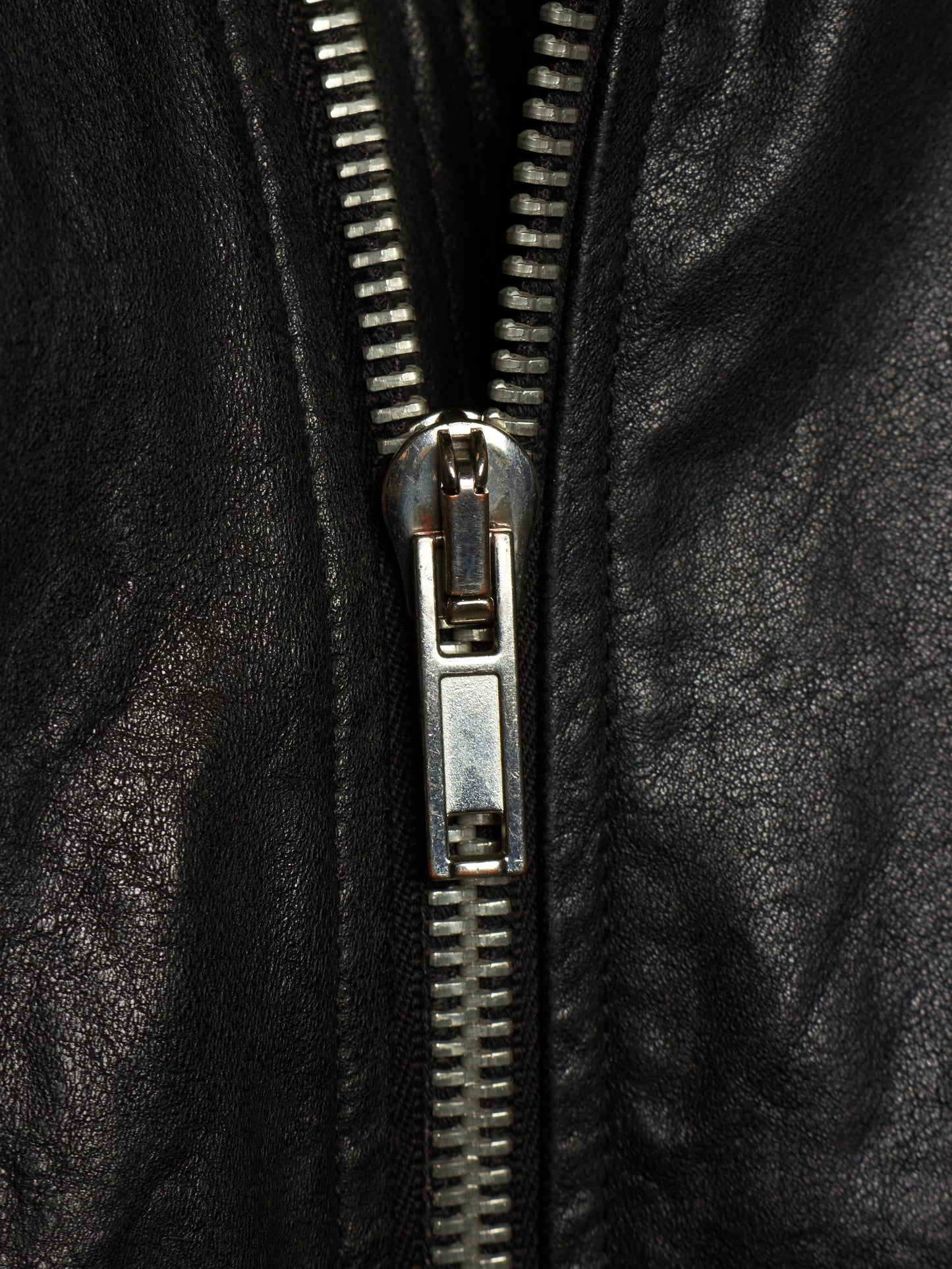 Close-up of a black leather jacket with a silver metal zipper running vertically down the center.