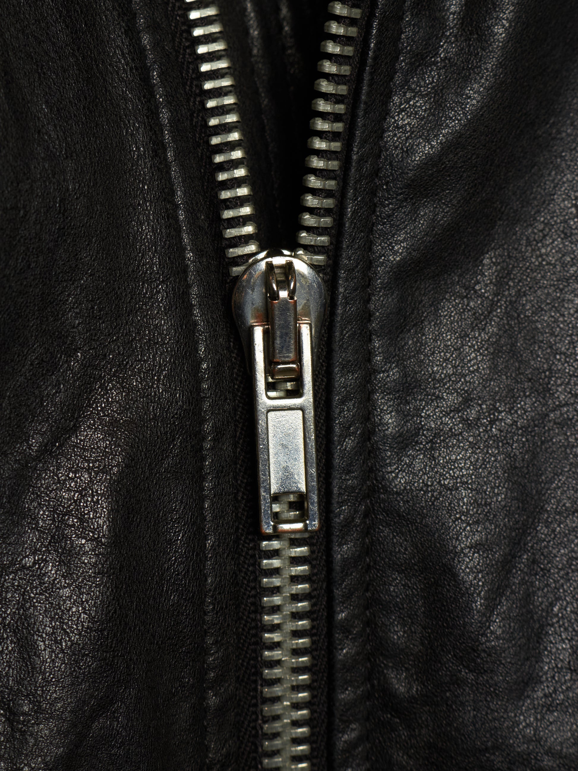 Close-up of a black leather jacket with a silver metal zipper running vertically down the center.