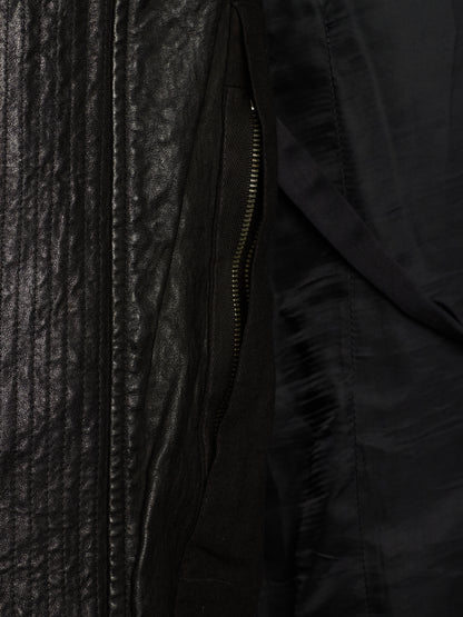 Close-up detail of a black jacket showing a textured leather-like panel, a black zipper, and a smooth black fabric interior.