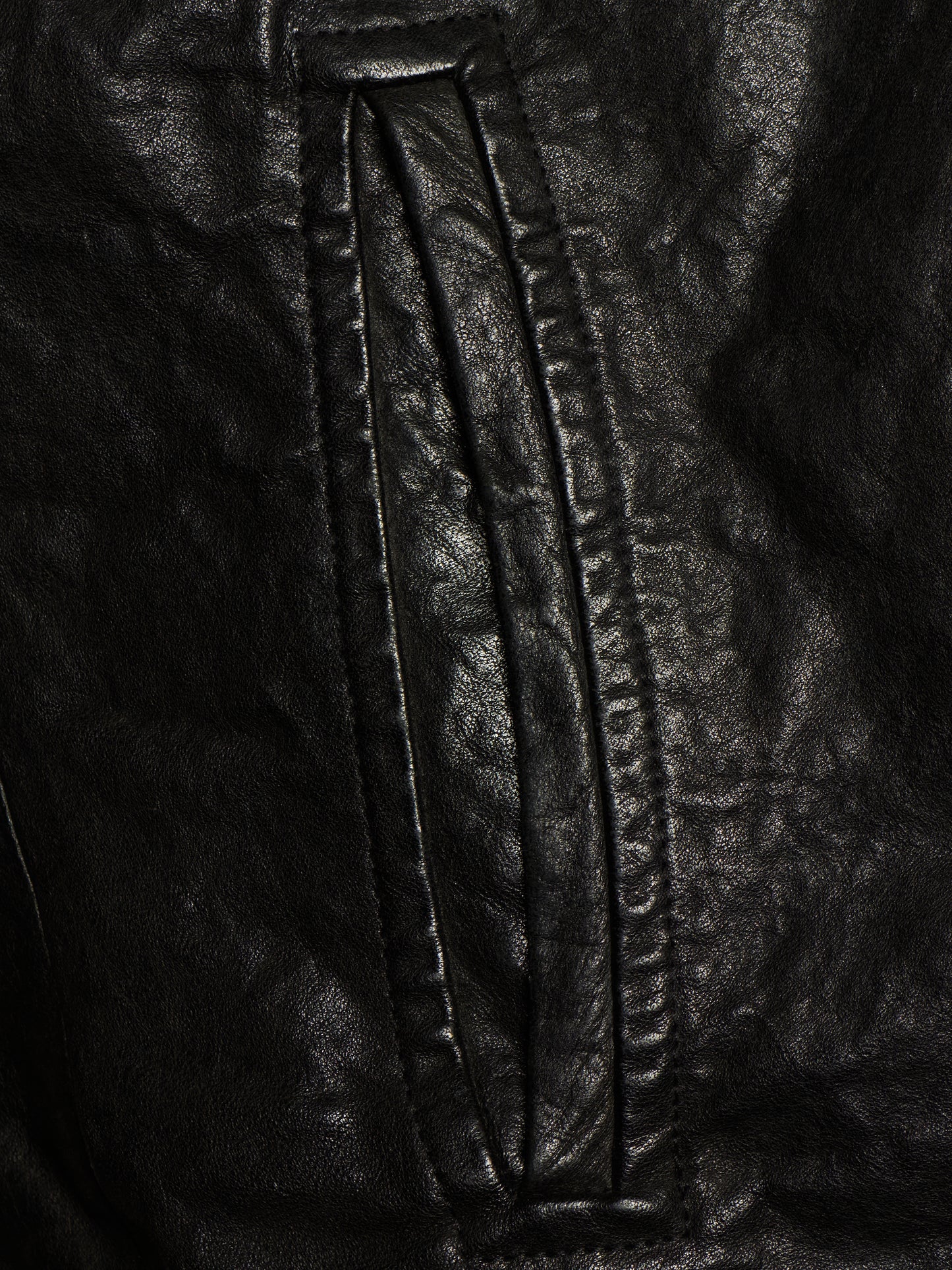 Close-up of a black leather jacket showing a vertical seam and stitched panel detail.