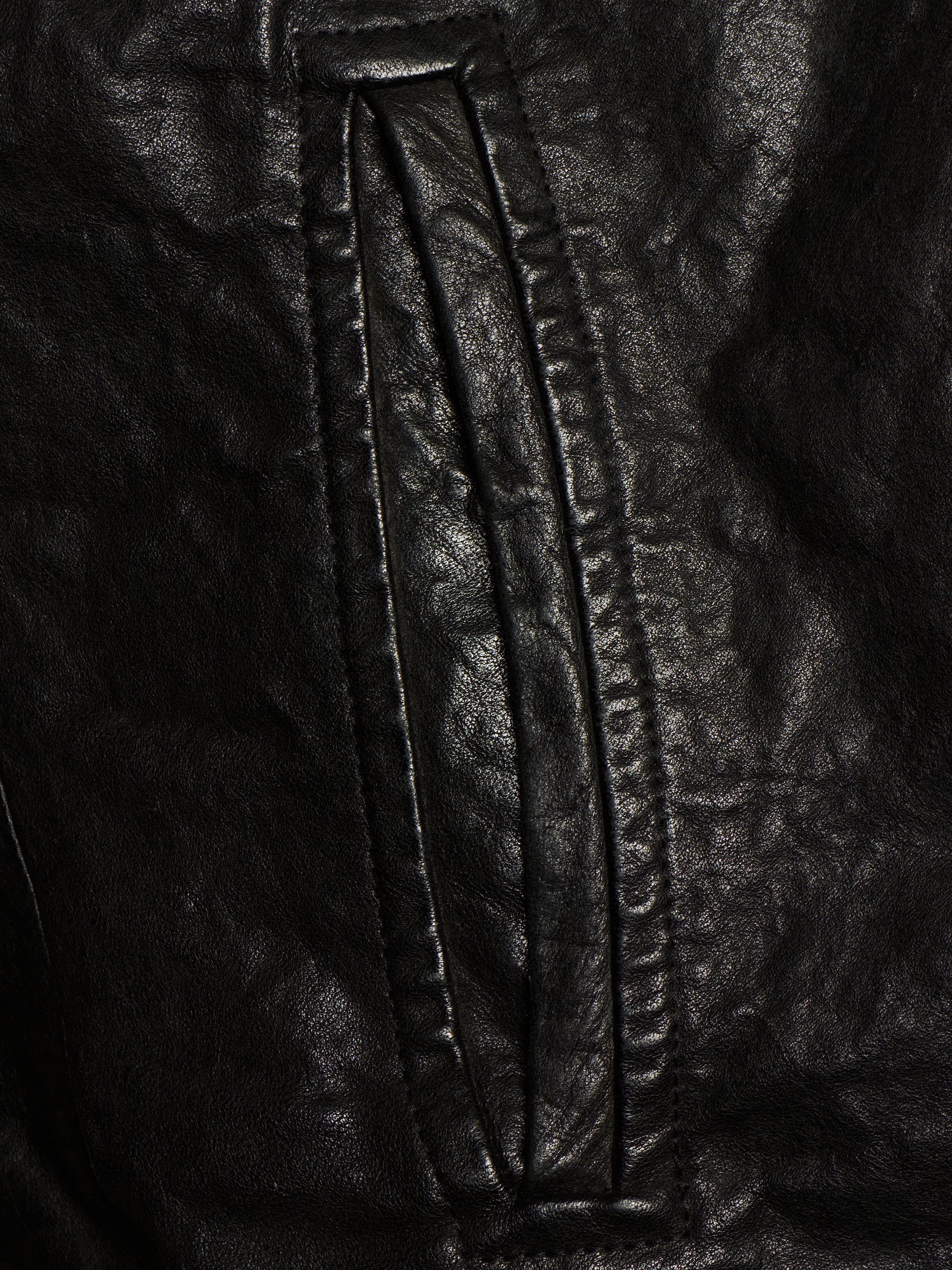 Close-up of a black leather jacket showing a vertical seam and stitched panel detail.