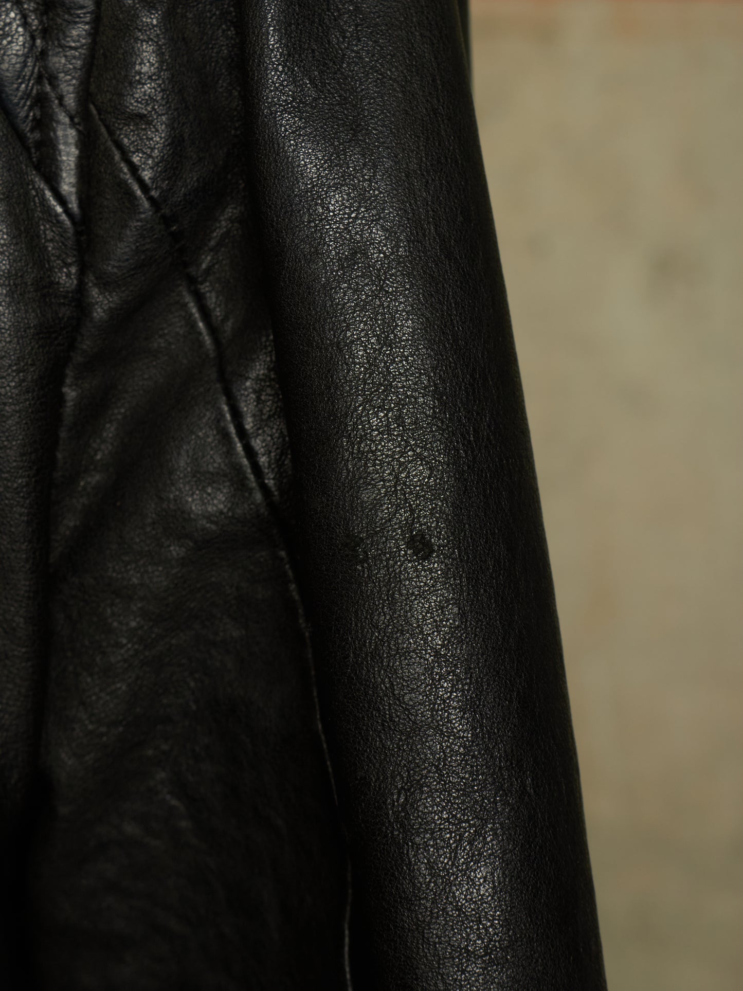 Close-up of a black leather jacket showing the textured grain and stitching detail.