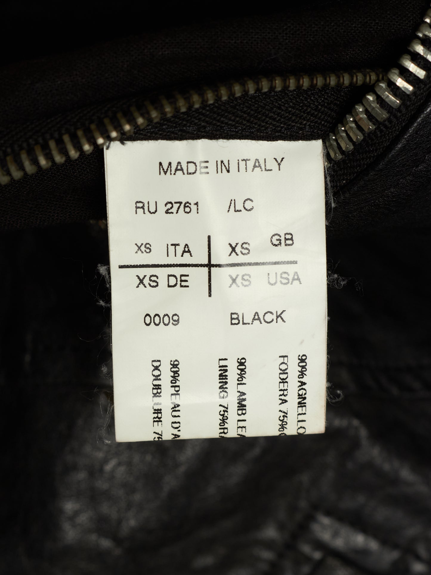 A close-up of a white size and material label sewn inside a black garment near the zipper. The label reads 'MADE IN ITALY', shows size information in Italian, English, German, and US, and indicates the fabric is 90% Angello and 70% polyamide, with 'BLACK' printed at the bottom.