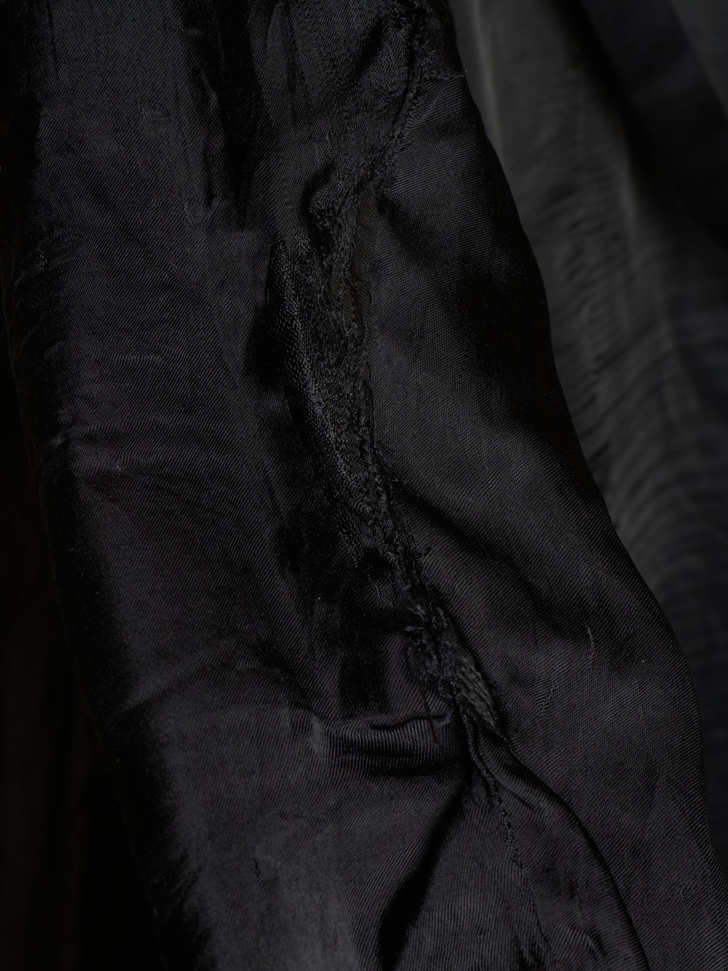Close-up of a black fabric garment or textile with visible folds, texture, and a slightly frayed edge.