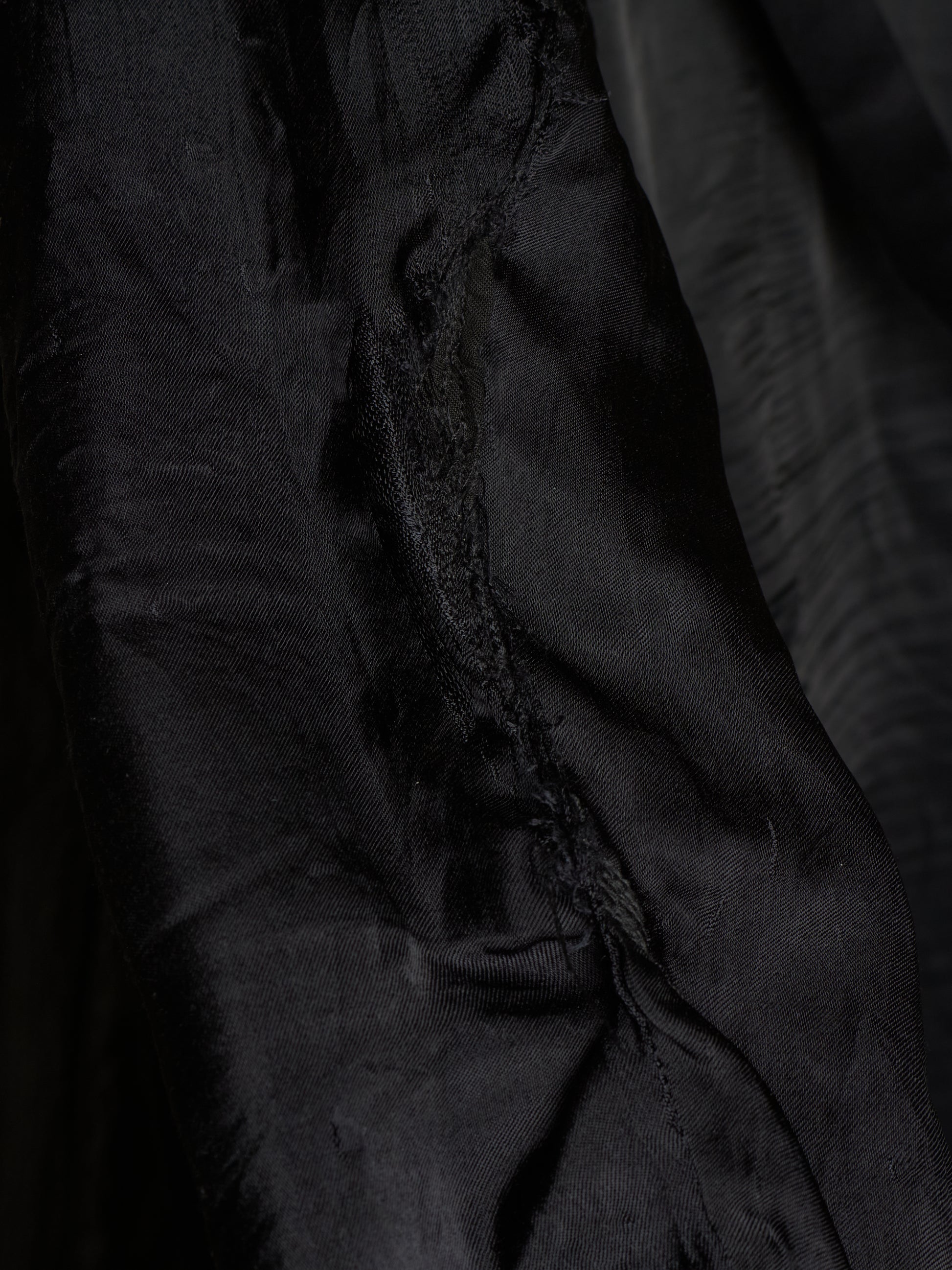 Close-up of a black fabric garment or textile with visible folds, texture, and a slightly frayed edge.