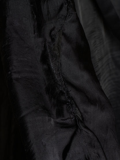 Close-up of a black fabric garment or textile with visible folds, texture, and a slightly frayed edge.