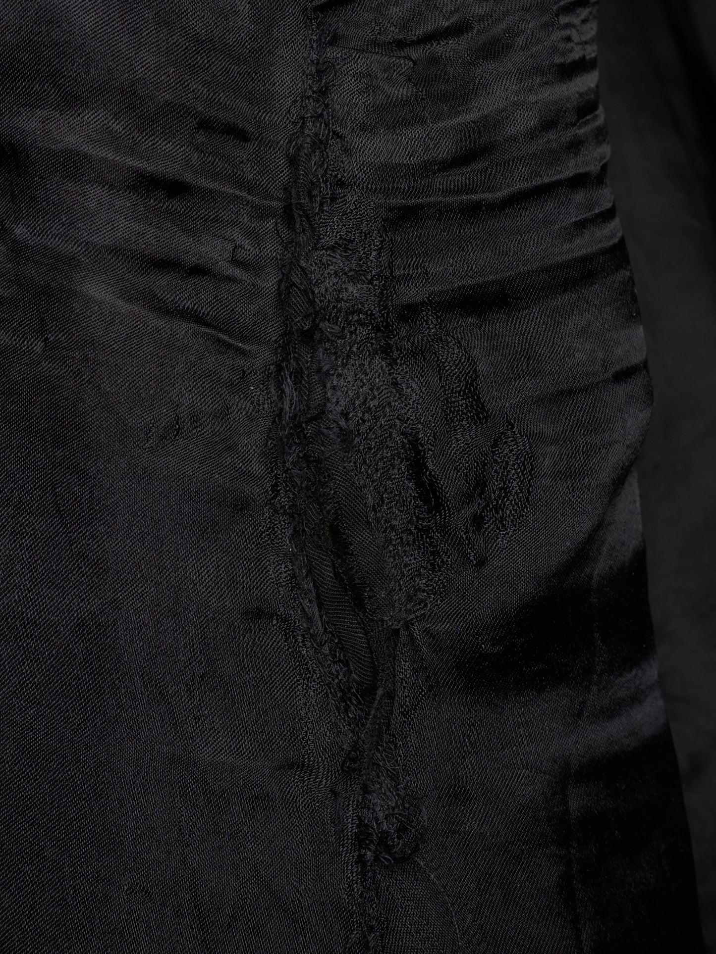 Close-up of a black textured fabric garment with gathered ruffles and a central seam detail.
