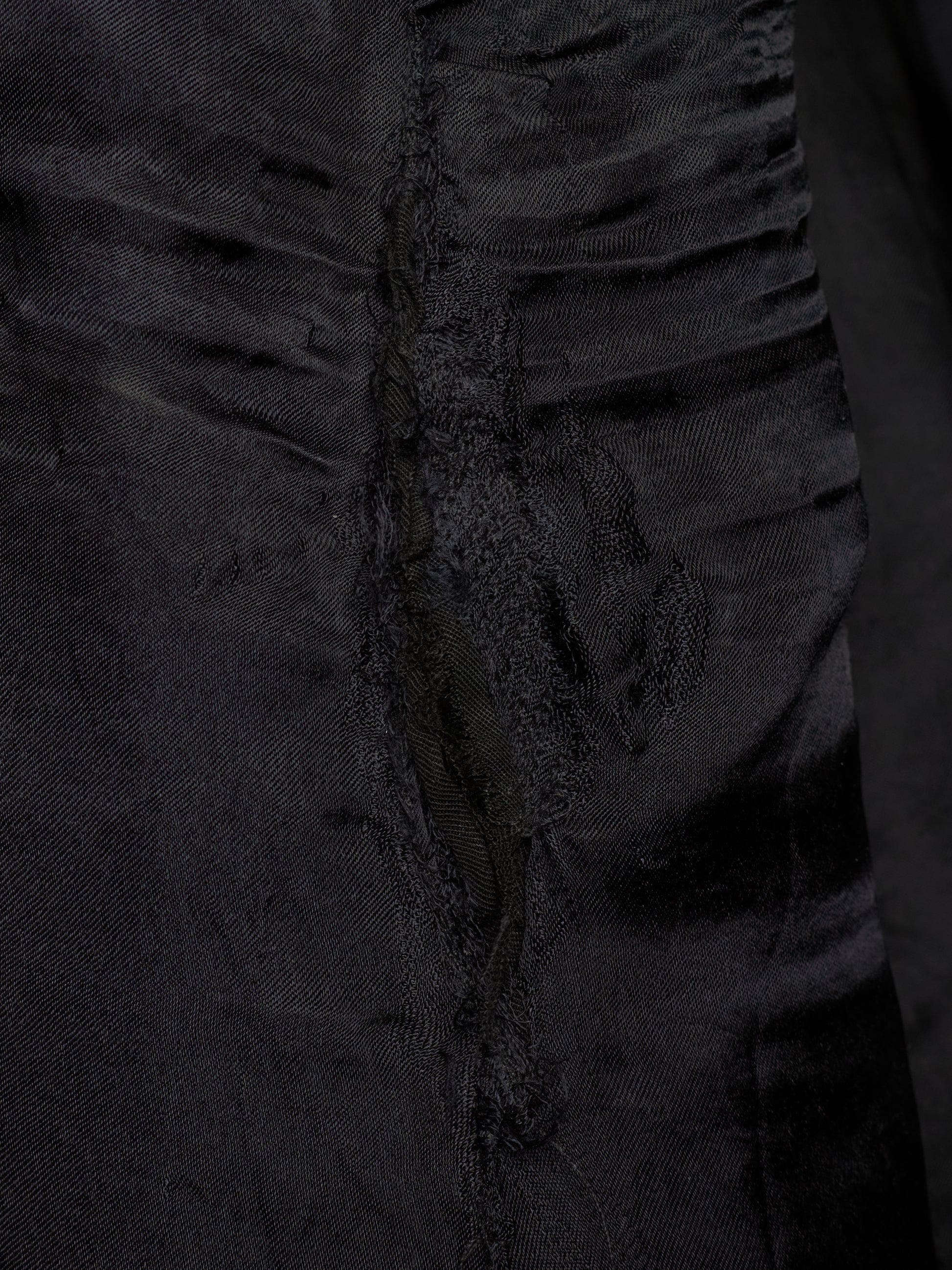 Close-up of a black textured fabric garment with gathered ruffles and a central seam detail.