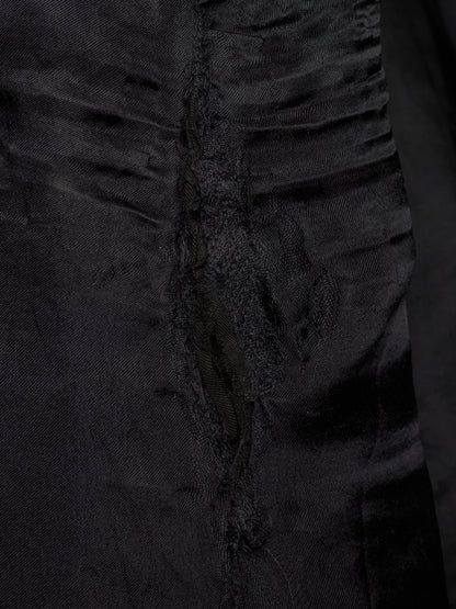 Close-up of a black textured fabric garment with gathered ruffles and a central seam detail.