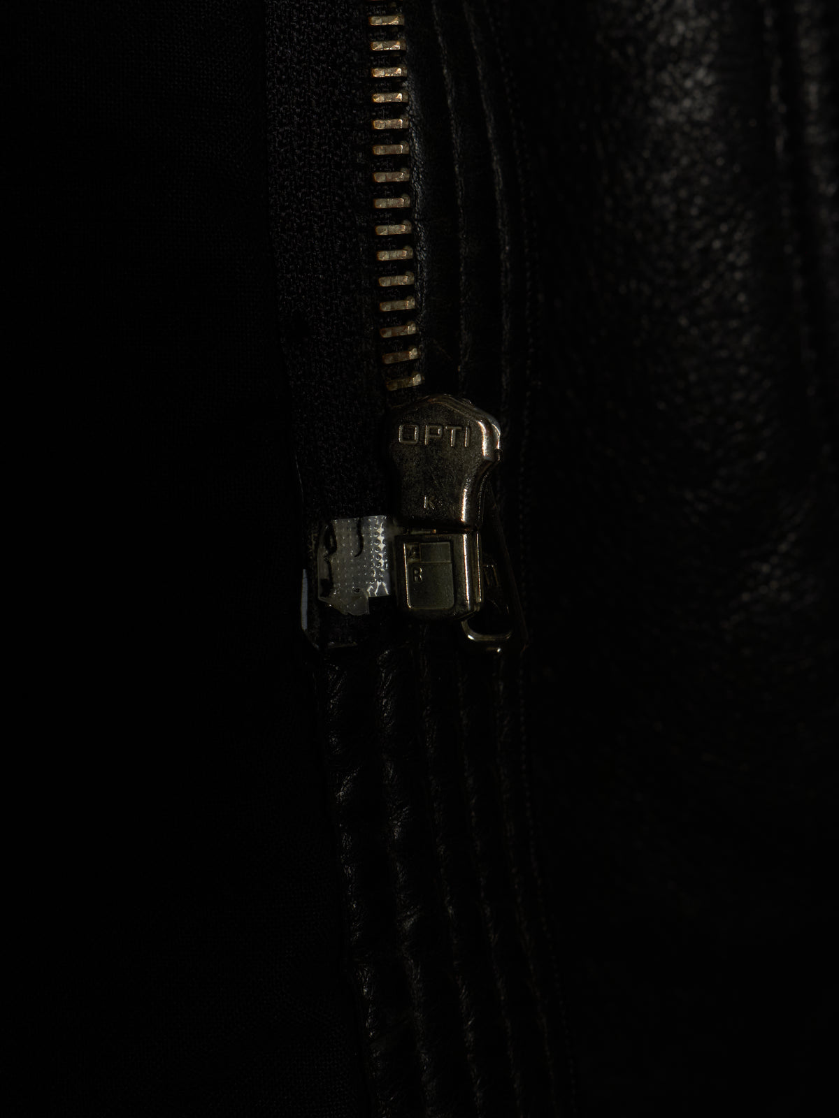 Close-up of a black leather zipper with a dark metallic pull tab on a black background.