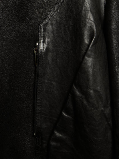 Close-up of a black leather jacket showing the textured leather material, a diagonal seam, and a dark metal zipper.