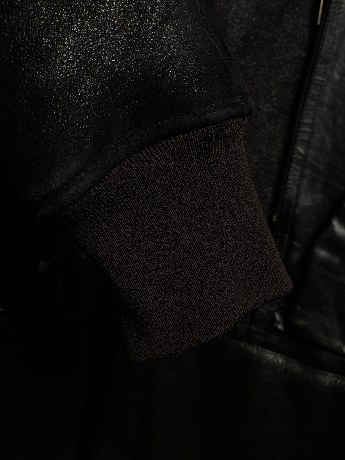 Close-up detail of a black jacket featuring a ribbed knit cuff and a textured leather or faux-leather sleeve.