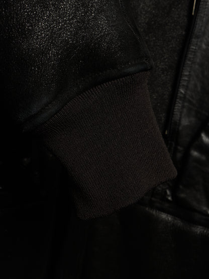 Close-up detail of a black jacket featuring a ribbed knit cuff and a textured leather or faux-leather sleeve.