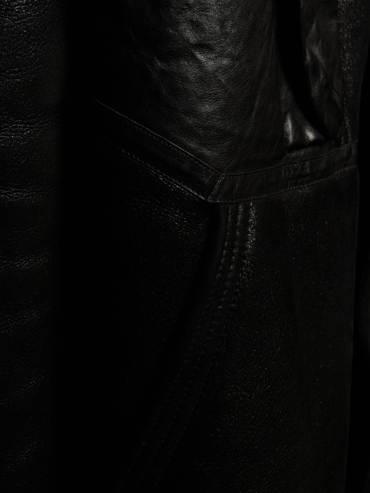 Close-up detail of a black leather garment, showing the texture of the leather and a stitched seam.