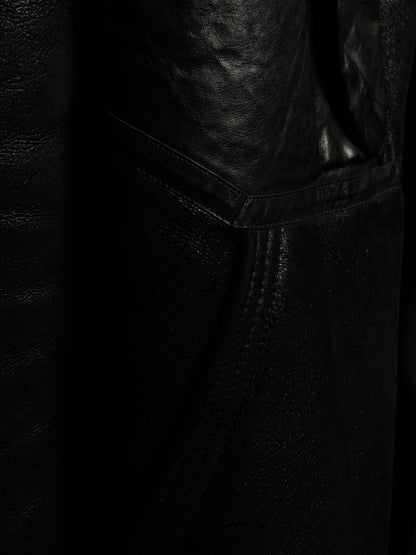 Close-up detail of a black leather garment, showing the texture of the leather and a stitched seam.