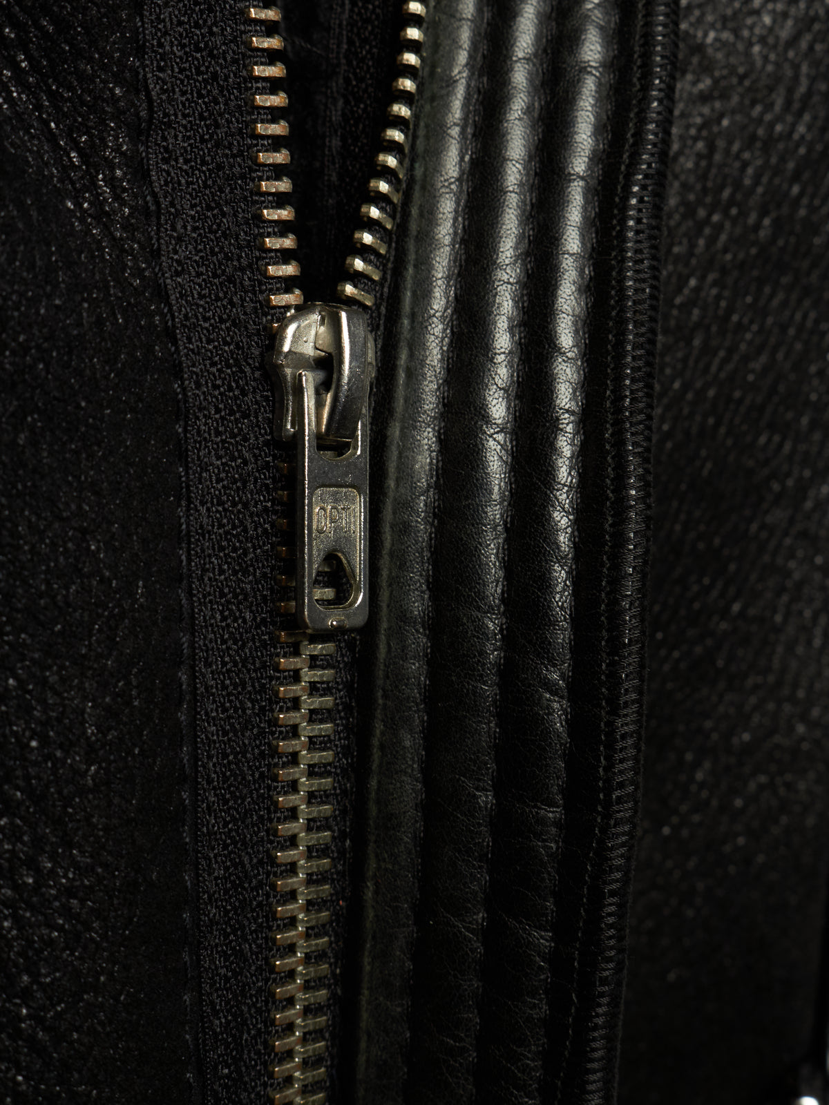 Close-up detail of a black textured leather zipper with a silver metal pull tab on a black leather garment.