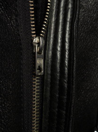 Close-up detail of a black textured leather zipper with a silver metal pull tab on a black leather garment.