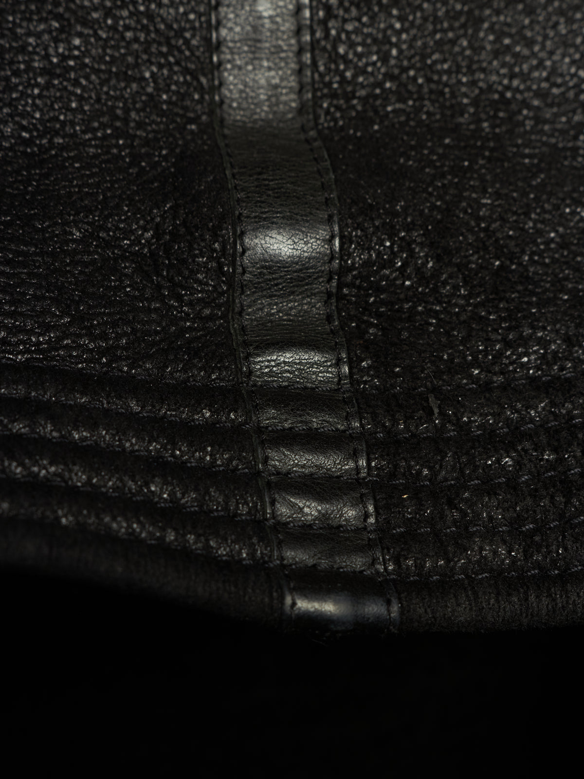 Close-up of black textured leather with a central stitched seam and horizontal stitched detailing.