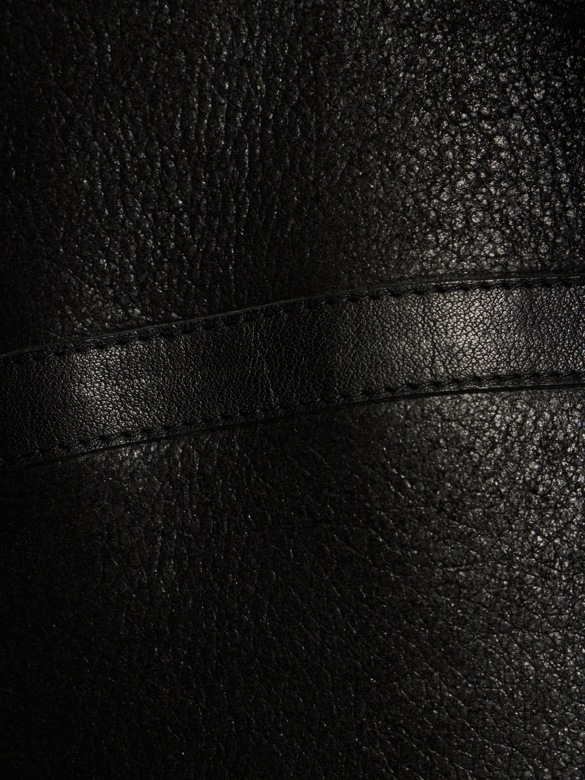 Close-up of black textured leather with a horizontal stitched seam.