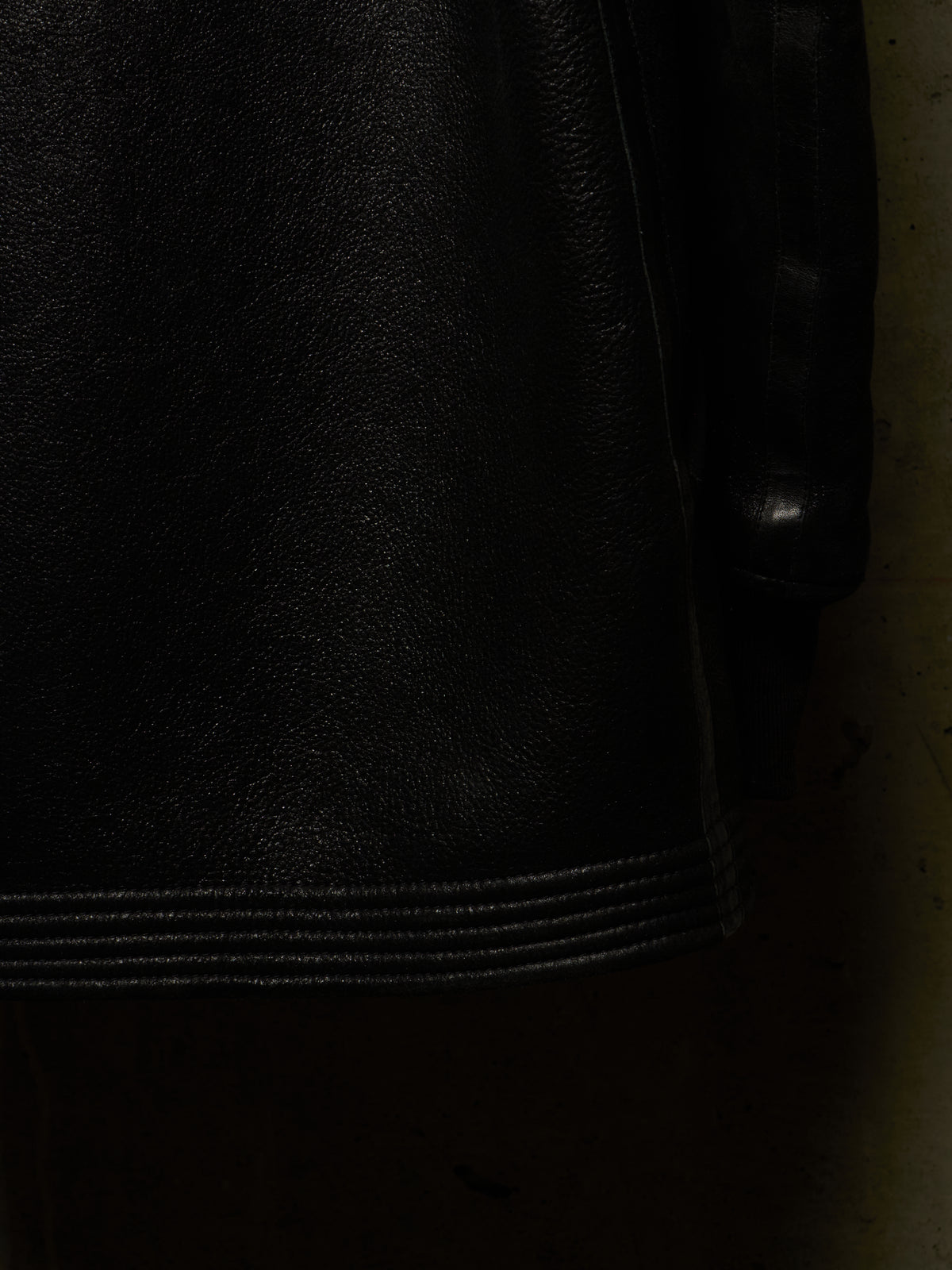 Close-up detail of a black leather jacket showing the texture of the leather and a stitched hem.