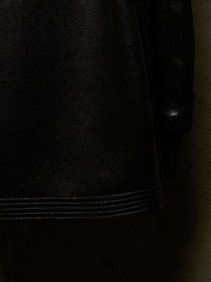 Close-up detail of a black leather jacket showing the texture of the leather and a stitched hem.