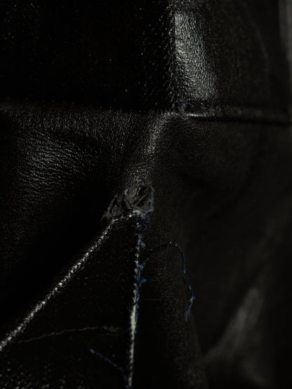 Close-up of a black leather item showing a small tear or hole near the center, with visible thread and dark textured material around it.