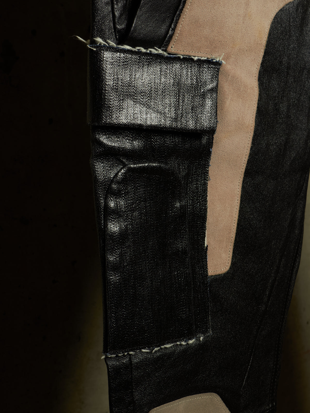 Close-up of a black textured leather or faux-leather garment with contrast beige lining and visible raw stitching.