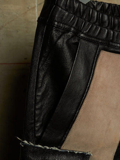 Close-up of black leather pants with a beige suede panel and a frayed denim hem detail.