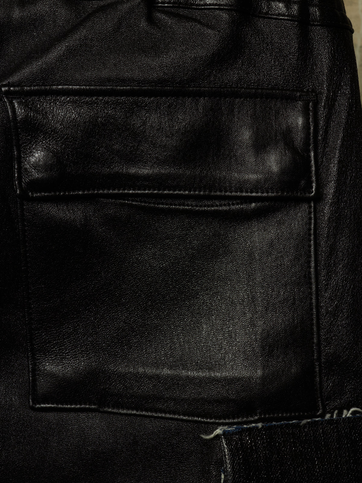 Close-up of a black leather jacket showing a front flap pocket with visible stitching and a textured leather surface.