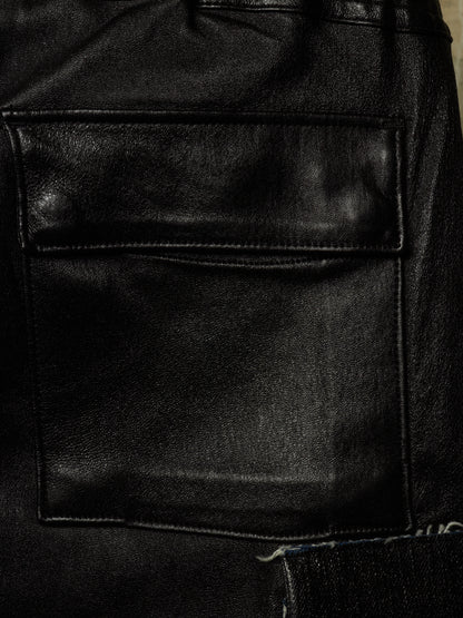 Close-up of a black leather jacket showing a front flap pocket with visible stitching and a textured leather surface.