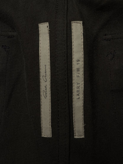 Close-up of a black jacket or coat showing two vertical light gray labels stitched on the front, with one label featuring a signature and the other reading 'LARRY F/W 18' and 'SANTA MONICA'.
