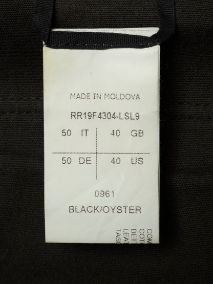 A close-up of a white paper garment tag sewn onto a black fabric item. The tag shows printed text including 'MADE IN MOLDOVA', a product code, weight and size markings, and 'BLACK/OYSTER' at the bottom.