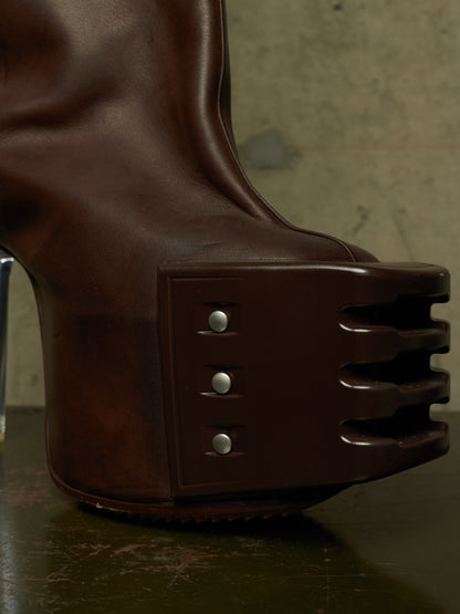 A close-up of a dark brown leather boot with a highly sculptural, ribbed platform sole and three silver rivets on the side.