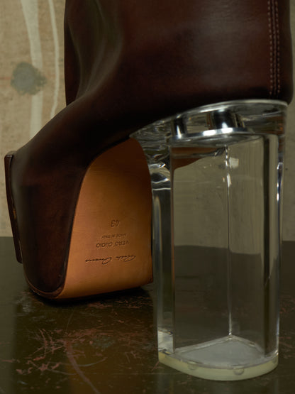 A close-up of a dark brown leather high-heeled shoe with a clear glass block heel, showing the tan leather insole with 'DIODO DESIGN' branding.