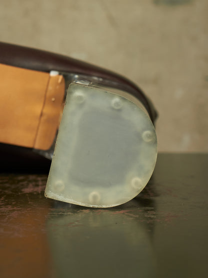 A close-up of a translucent, semi-opaque rubber or plastic protective pad with circular raised bumps, attached to a dark brown and tan object on a dark reflective surface.