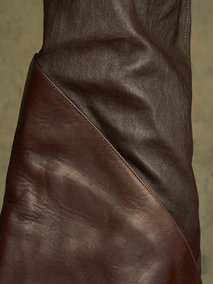 Close-up of a dark brown leather garment, showing the texture and diagonal seam against a neutral background.