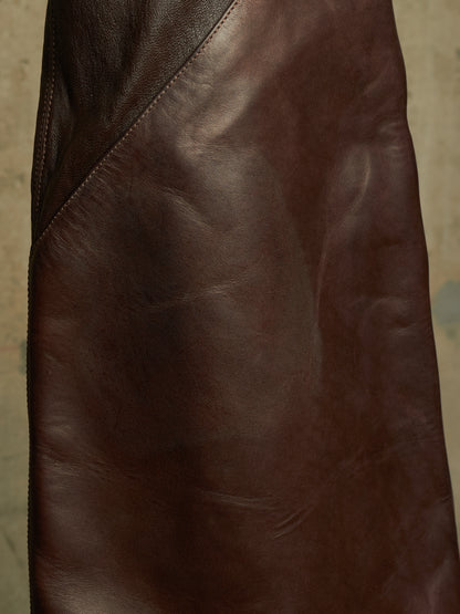 A close-up of a dark brown leather garment, showing the smooth texture and diagonal seam stitching.