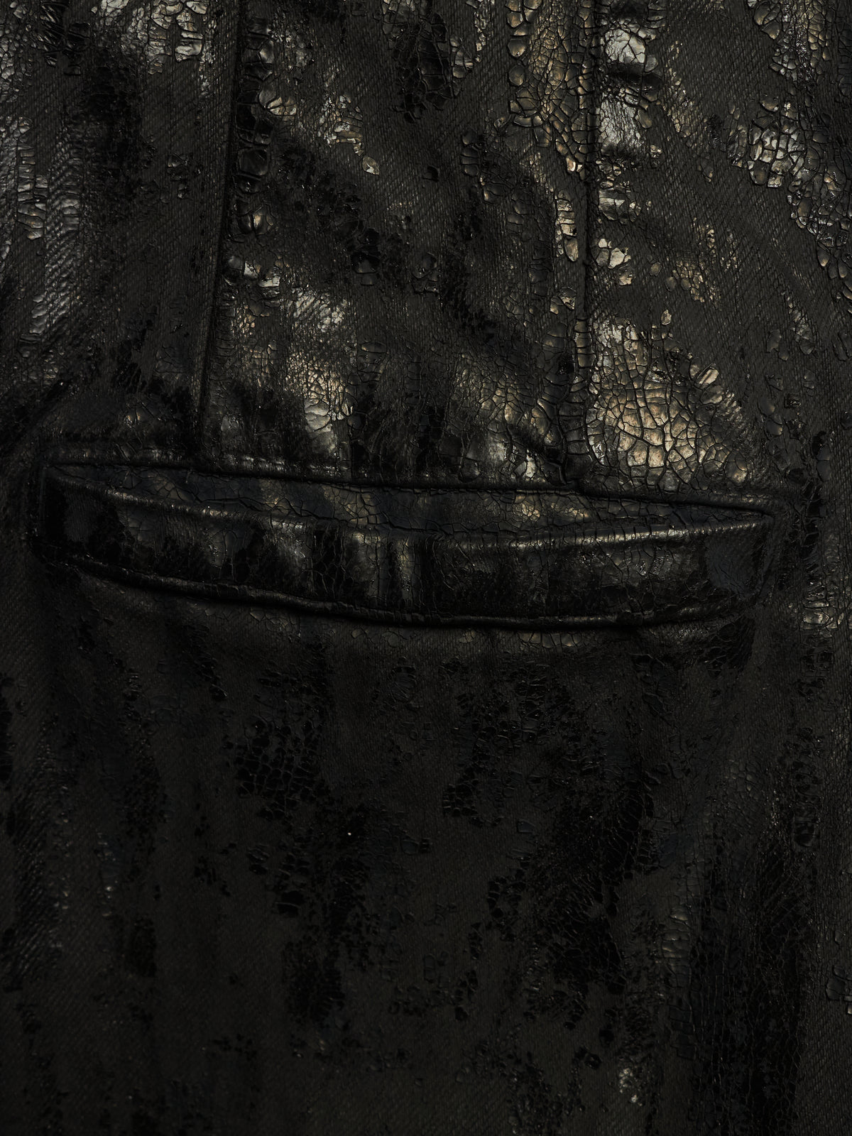 Close-up of a black textured fabric garment with a subtle reptile or crocodile-embossed pattern and a horizontal seam detail.