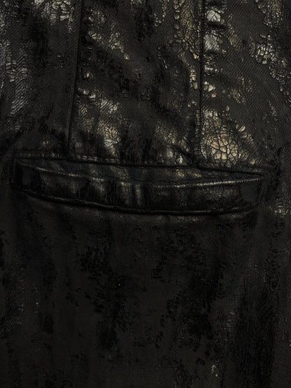 Close-up of a black textured fabric garment with a subtle reptile or crocodile-embossed pattern and a horizontal seam detail.