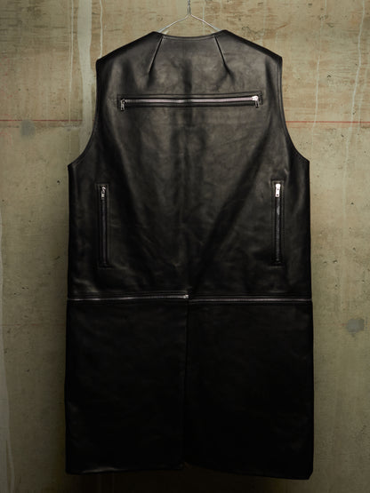 A black leather sleeveless vest with silver zippers, hanging on a wire hanger against a textured concrete wall.