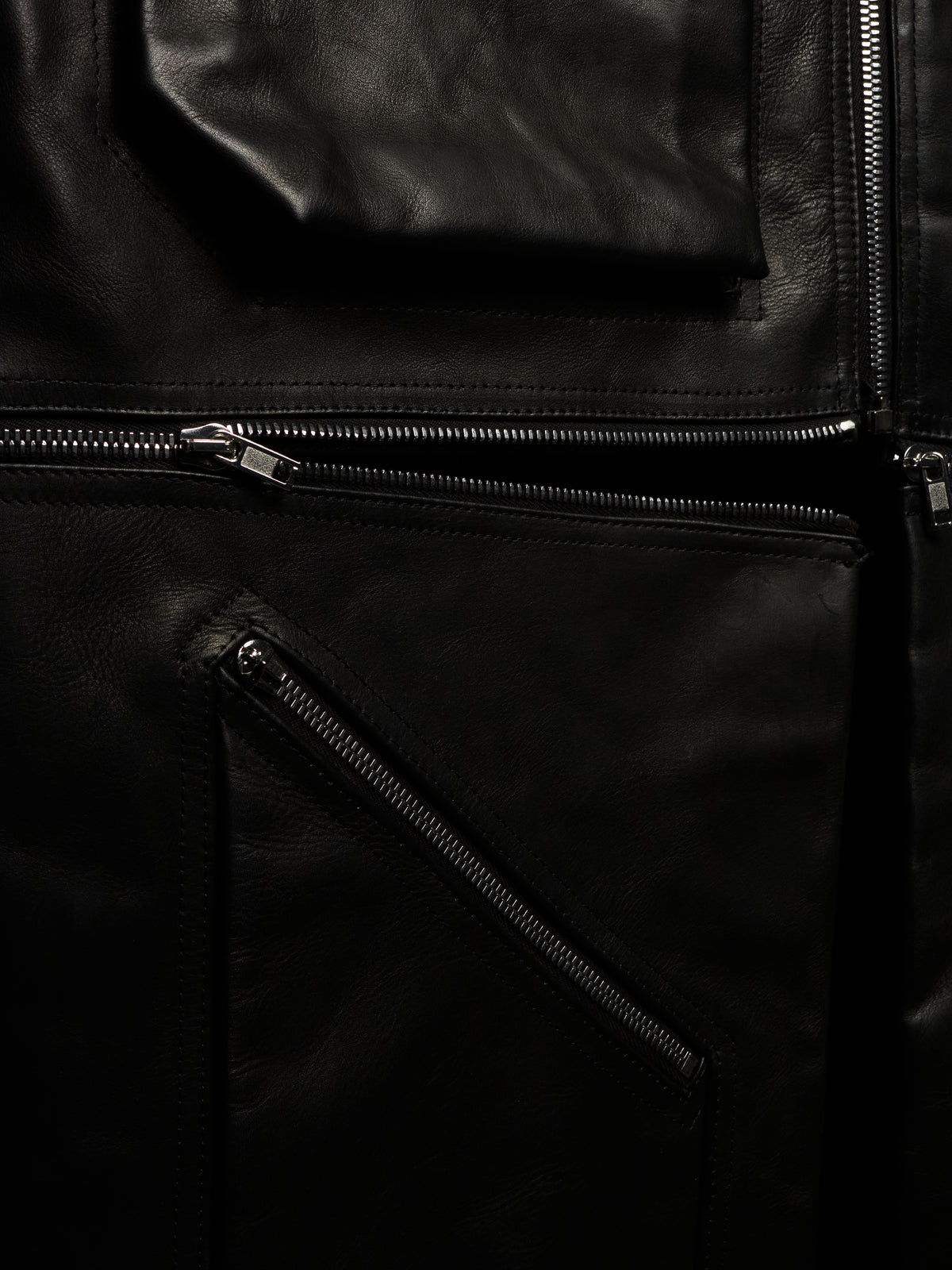 Close-up of a black leather jacket with multiple zippered pockets and silver-toned metal zippers.