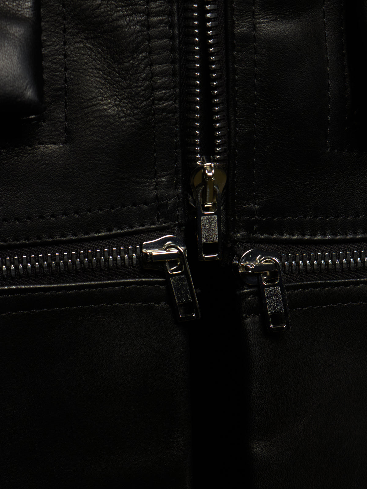 Close-up detail of a black leather jacket showing silver metal zippers and stitching.