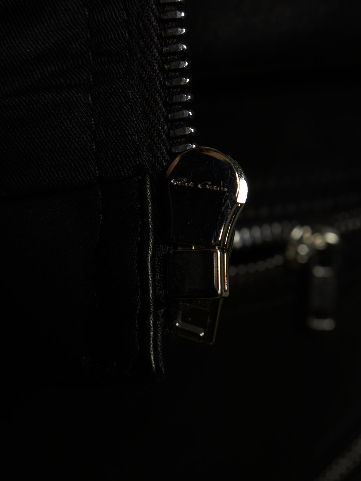 Close-up of a black zipper with a polished metallic pull tab engraved with the brand name 'Ghili & Ghili'.