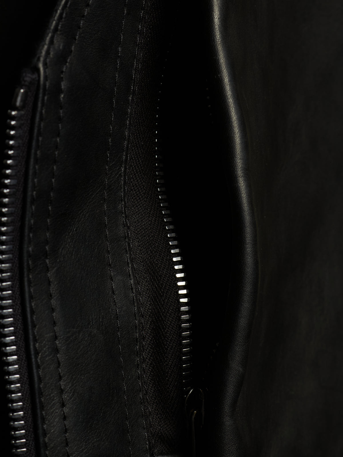 Close-up detail of a black leather or faux-leather bag showing a zipper, stitching, and textured material.
