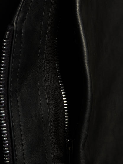 Close-up detail of a black leather or faux-leather bag showing a zipper, stitching, and textured material.