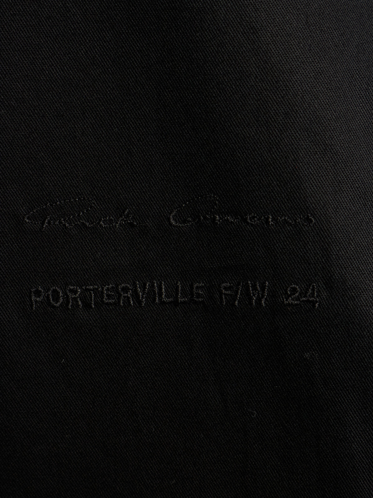 Close-up of a black fabric surface with tonal embroidered text reading 'Giorgio Armani' and 'PORTERVILLE F/W 24'.