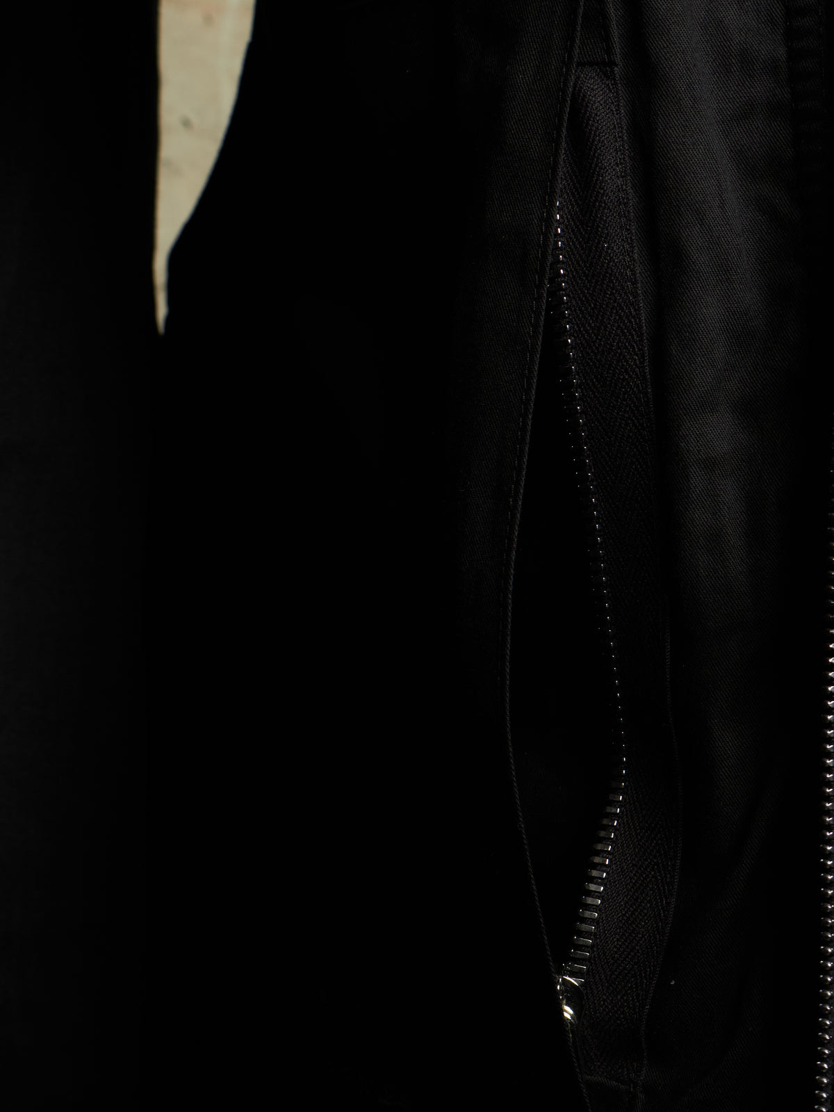 Close-up detail of a black jacket showing a black zipper track and textured fabric.